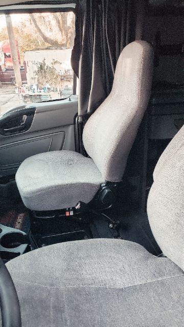 Truck interior showing driver's seat and adjacent passenger seat with light gray fabric. Steering column and door panel visible.