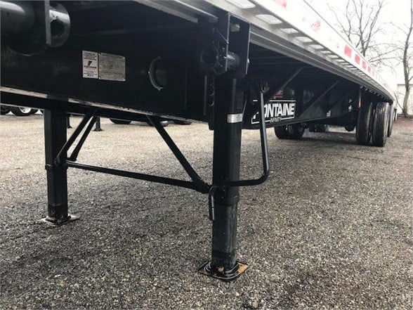 Fontaine INFINITY flatbed trailer with landing gear leg and support rails visible, stock number 562433, in-service area on a paved lot.