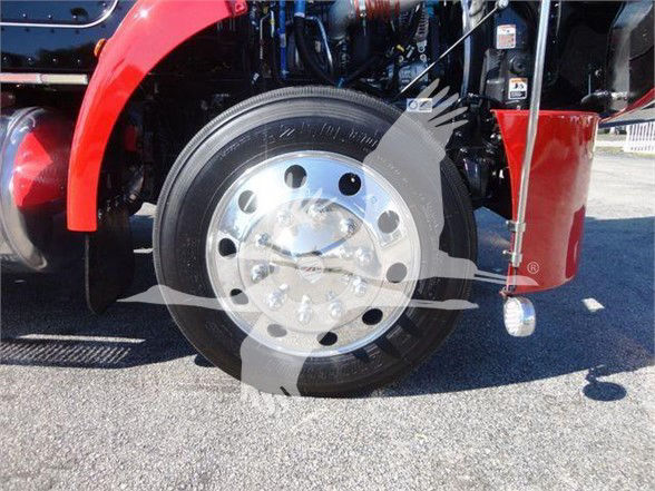 Front wheel of a 2022 Peterbilt 337 with red fender and chrome wheel centerpiece, partial engine bay components visible.