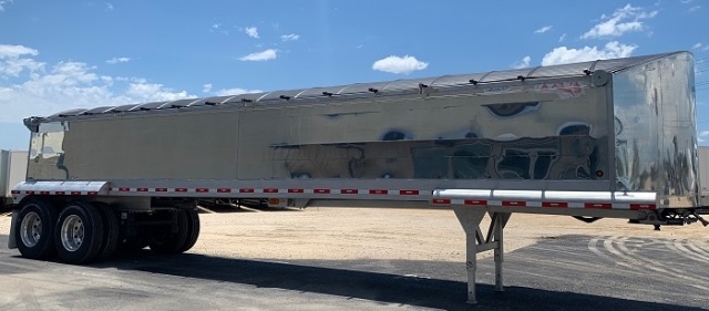 aluminum end dump trailer in a parking lot showing a long rectangular steel body with a rear hinge and dual-axle wheels.