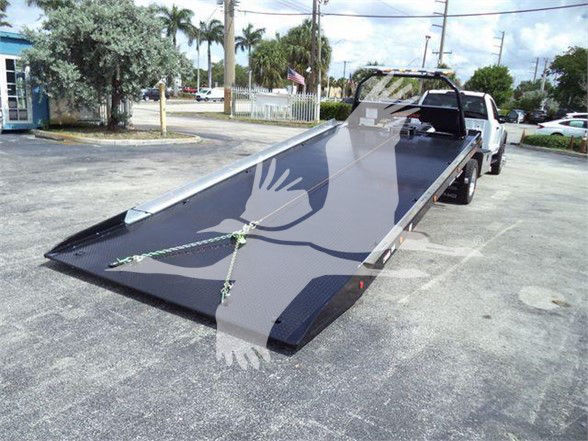 Flatbed tow truck with a long lowered bed extended on the ground. visible text: none legible; generic scene.