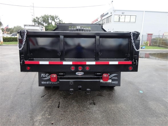 Ram 3500 dump truck bed rear view in a dealership lot with red/white reflective tape and chains on both sides.