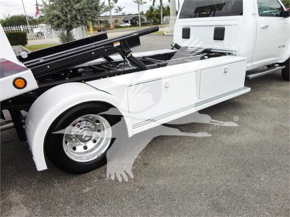 Ram 5500 HD tow truck body with service/storage compartments and white paint; front wheel visible; part of cab in background.