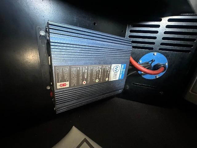 Conventional sleeper truck interior with blue power inverter mounted and connected by red cables to a blue circular access port.