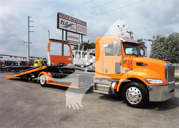Peterbilt 337 tow truck with orange cab and flatbed, stock number J06176, front grille chrome, dealership lot in background.