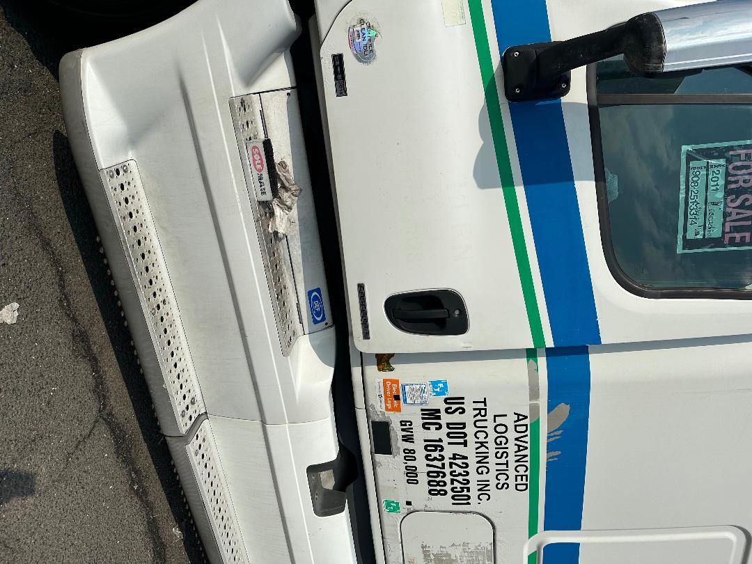 Truck door area with decals and labels: Advanced Logistics, US DOT 42350, MC 1637688, GVW 80,000, and blue/green stripe on white Freightliner Cascadia sleeper cab.