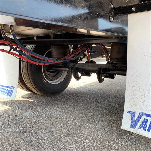 Flatbed trailer undercarriage showing dual rear suspension, axle, and wiring; Vanguard branding on mudflap; wheel and tire visible.