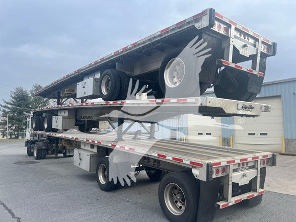 2015 Benson aluminum flatbed trailer being loaded onto a multi-axle trailer, showing steel frame, wheels, and reflective tape.