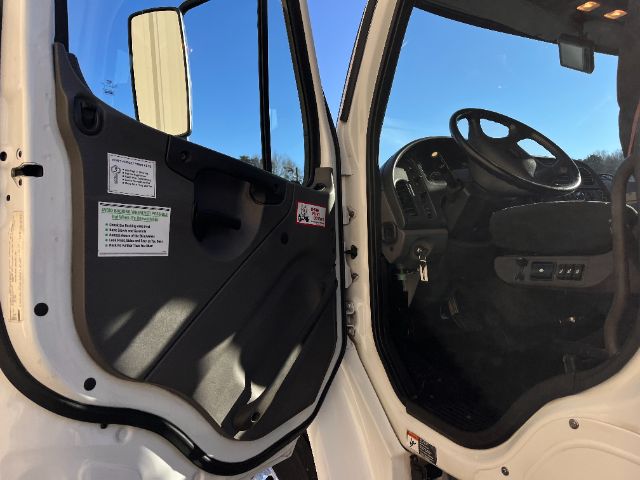 Cab interior of a 2015 Freightliner M2 with open driver's door; steering wheel and dashboard visible; stickers on door panel.
