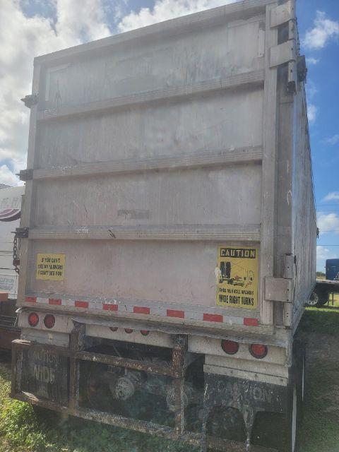 Back view of a Warren WHDT48x102-2-AS walking floor trailer with yellow caution stickers on the rear doors and tail lights. Weathered metal panels and mud flaps visible.