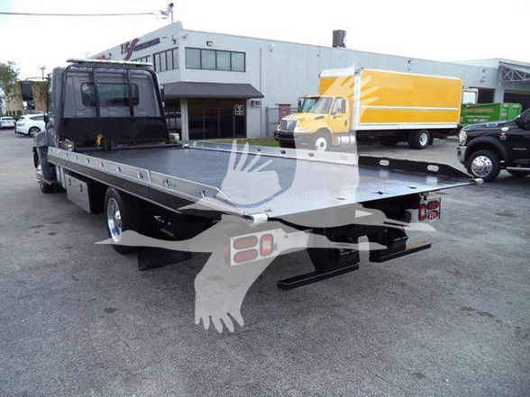 2014 Hino 258ALP tow truck flatbed rear view showing long aluminum bed and wheel-lift, with company building in background.