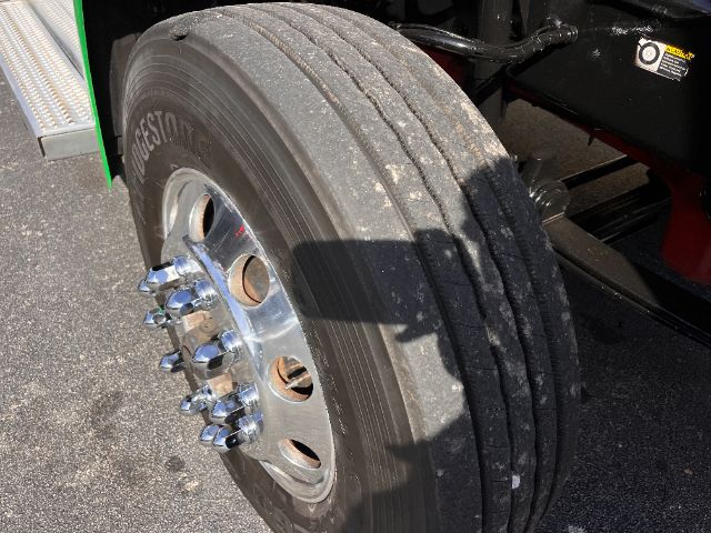 Front wheel of a Peterbilt 579 daycab showing Bridgestone tire with chrome hub and lug nuts; part of the truck chassis visible.