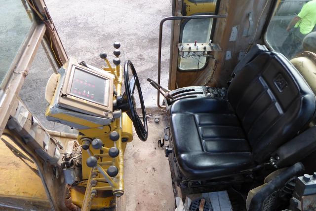 Caterpillar 16G grader cab interior with control panel, joystick levers, and operator seat seen from left side.