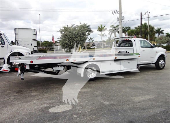 Flatbed tow truck with extended white cab and aluminum flatbed, side mirrors, lights, and a hitch visible.