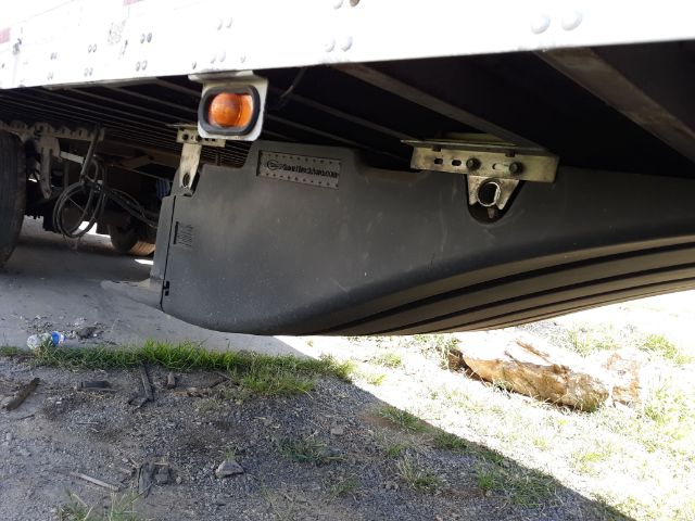 Underbody of a trailer showing a plastic sway panel with a small metal plate and an orange reflector. Visible text on a metal plate reads '...M...'.