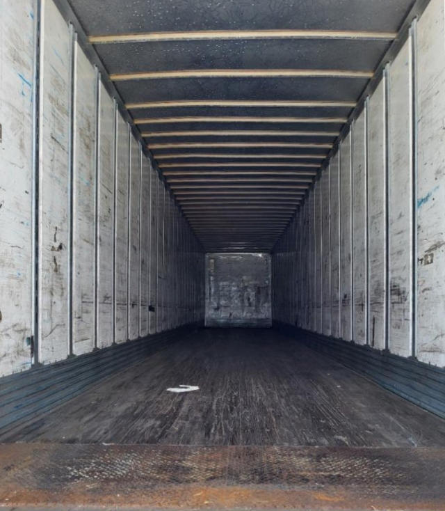 Trailer interior showing long rectangular cargo space with metal side walls and a wooden floor. End wall visible; no obvious branding in view.