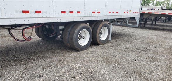 Trailer with dual rear axles showing white dry van with red reflective tape and undercarriage components visible.