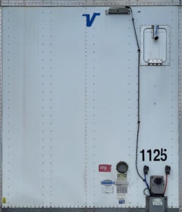 Rear view of a white Vanguard VXP trailer door with blue Vanguard logo, VIN/sticker area, and electrical/yoke components visible.