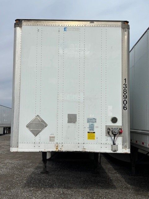 Rear view of a 2013 Stoughton 53' dry van trailer with vertical registration number 138906, various placards, and a diamond-shaped hazard sign.