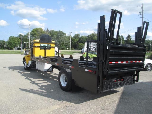 Kenworth T300 flatbed truck with black utility bed and raised side ramps, yellow cab, empty flatbed area, rear view