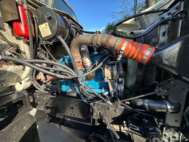 Engine bay with turquoise/blue engine block visible, black hoses, metallic pipes, orange ribbed hose, and various wiring harnesses.
