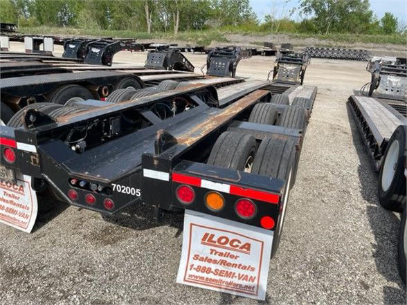 Lowboy trailer chassis with magnitudes and labels. Visible text includes 702005 on frame, taillights, and ILCOA trailer rentals sign.