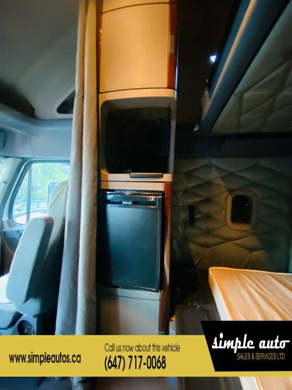 Cab interior of a Freightliner Cascadia showing a compact refrigerator and storage cabinets in the cab area.
