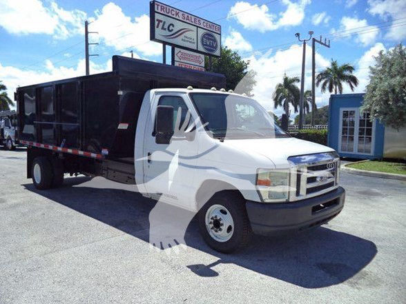 2011 Ford E450 dump truck with white cab and black dump body, side view parked at dealership lot.