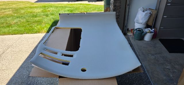 Vehicle hood with cutouts placed on cardboard in driveway. Appears to be light gray/blue primer with openings for windshield wipers and vents.