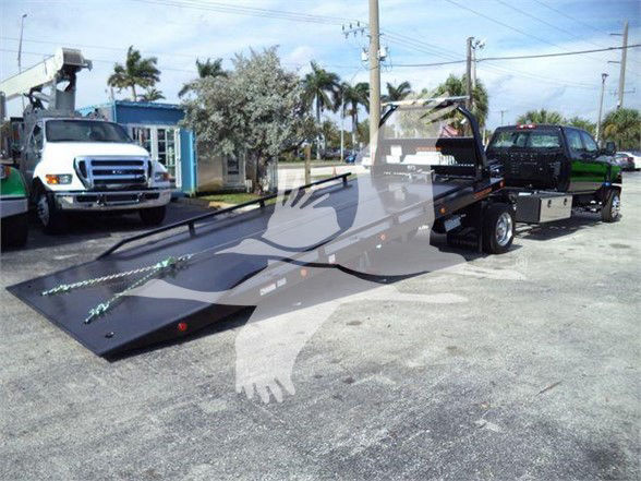 Tow truck with a long low-profile flatbed trailer attached, in a parking lot.