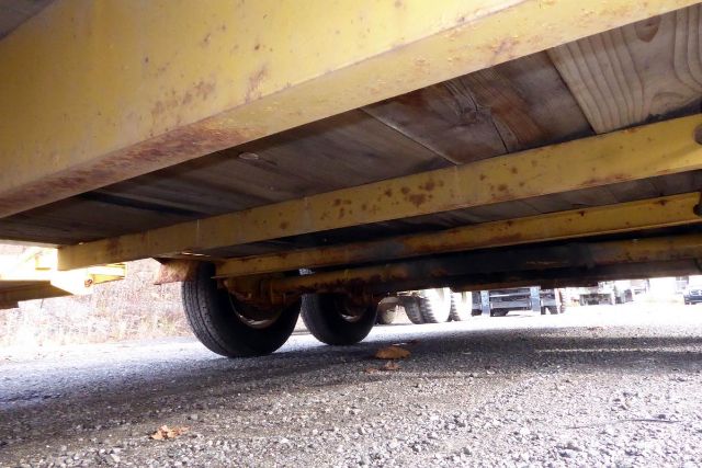 Trailer underside showing wheels and frame with yellow support beams and gravel ground.