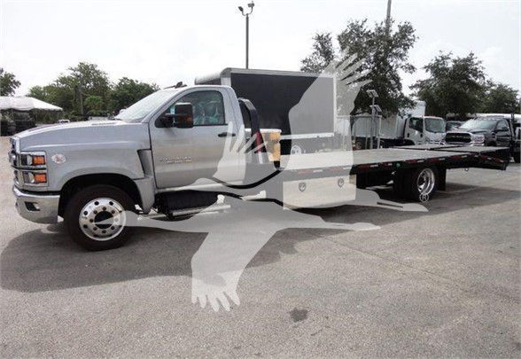 Chevrolet Silverado 6500HD flatbed tow truck in a dealership lot, side view with extended flatbed and dual rear wheels.