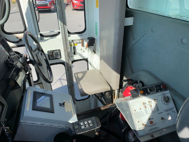 Interior of a 2006 International 4300 truck cab showing steering wheel, control panel, and seating with a gray operator chair. Dashboard touchscreen panel and control box with red fire extinguisher nearby.