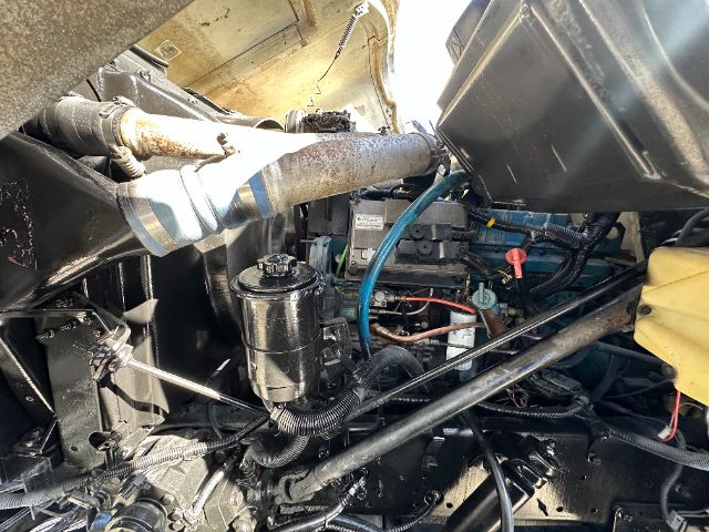 Engine bay of a 2000 International F-2554 vacuum truck showing hydraulic lines, coolant reservoir, and wiring.
