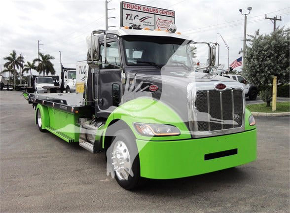 Peterbilt 337 tow truck in green and gray color with W900-style grille and flatbed cargo area.