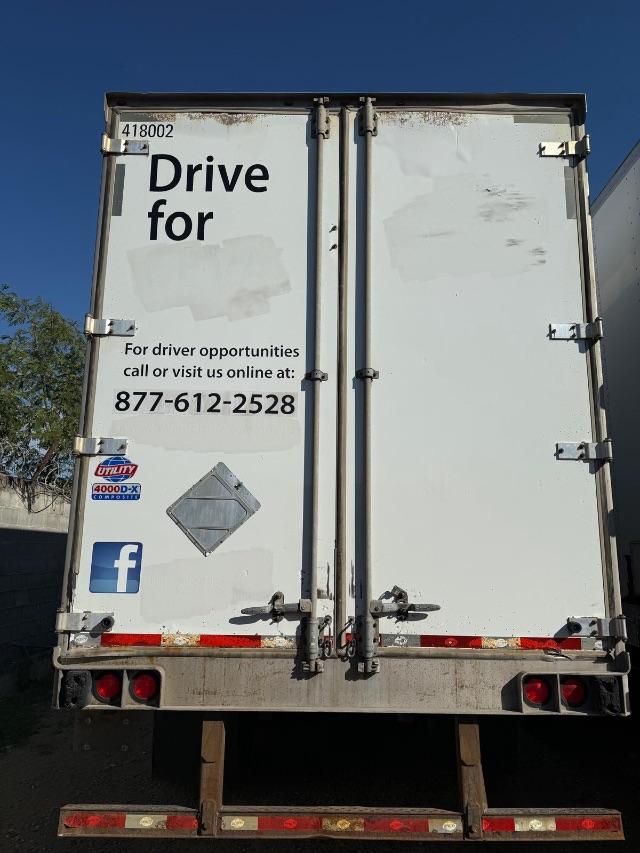 Back of a utility trailer with doors, promotional text and logos, including Drive for driver opportunities and a phone number, Utility 4000DX sticker, and Facebook icon.