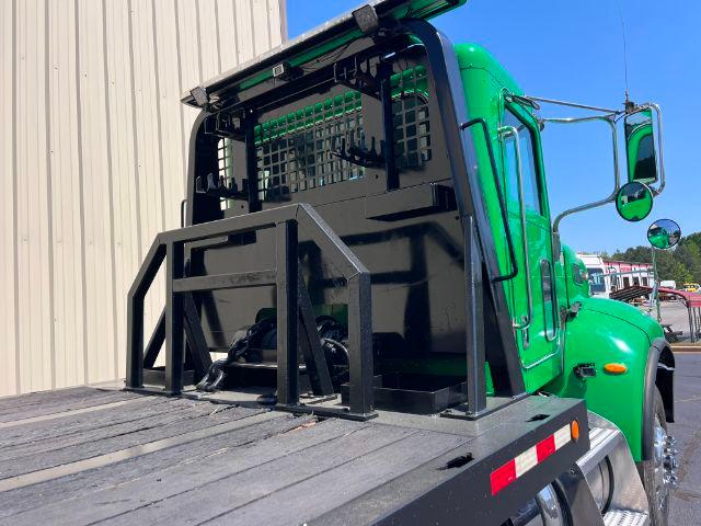 Green Peterbilt 348 rollback truck with a heavy-duty steel bed and rear loading equipment visible.