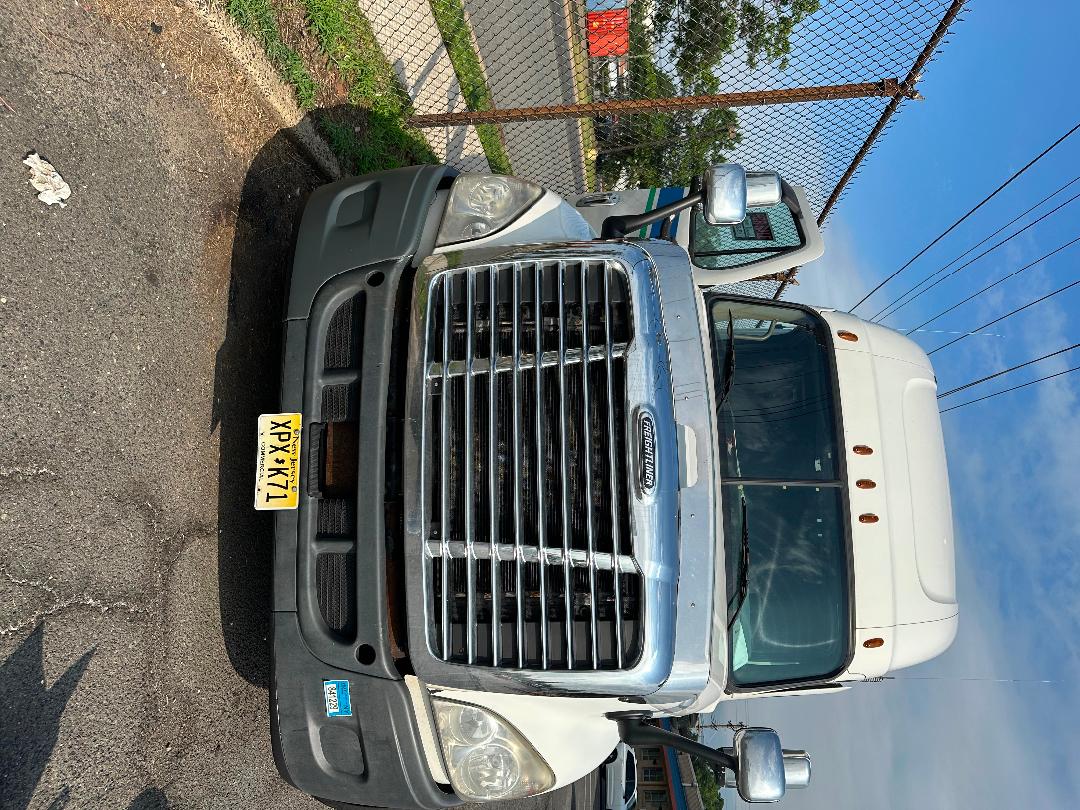 Freightliner Cascadia truck front view showing chrome grille, bumper, and New York license plate.