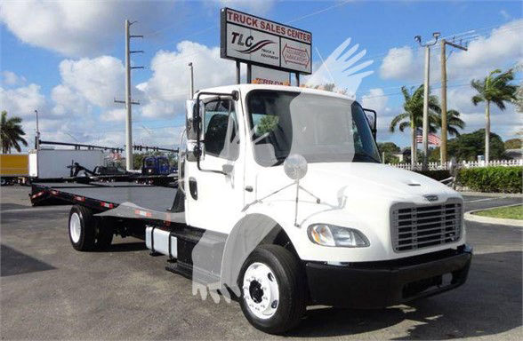 Flatbed tow truck by TLC sign in background with white Freightliner Business Class M2 106 cab and flatbed trailer.