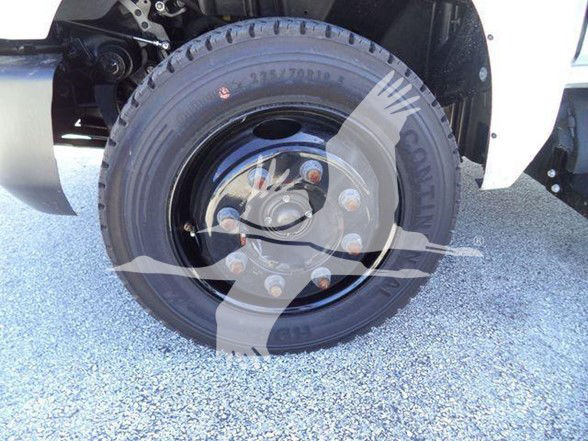 Truck front wheel shows steel rim with multiple lug nuts and tire, partial fender and suspension components.
