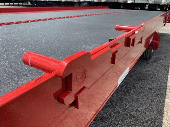 Red drop deck container delivery trailer single axle with stake pockets and frame detailing visible.
