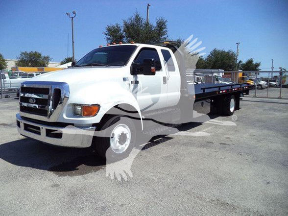 White Ford F-650 XLT flatbed tow truck with dual rear wheels, front grille and headlights visible, long flatbed with wheel chocks, truck cab in foreground.
