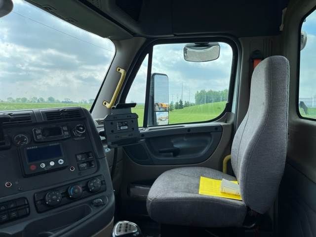 Cab interior of a 2015 Freightliner Cascadia truck showing driver seat and dashboard, VIN 1FUJGBDV6FLGE8667, stock GE8667, conventional daycab.