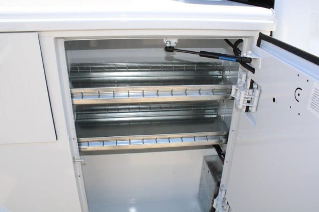 Open under-counter refrigerator or freezer with multiple wire racks and thermostat control visible on door.