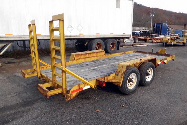Trailer with dual-axle platform and ramps, yellow paint, loaded desolate storage yard.