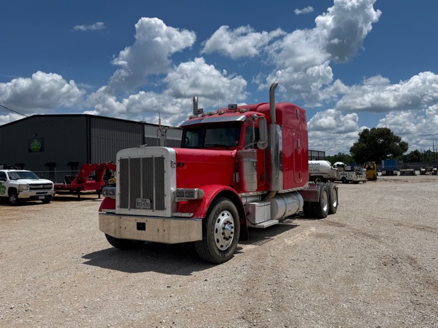 Peterbilt 379 tractor in red with sleeper cab, front grille, dual exhaust stacks, and chrome bumper in a gravel lot.