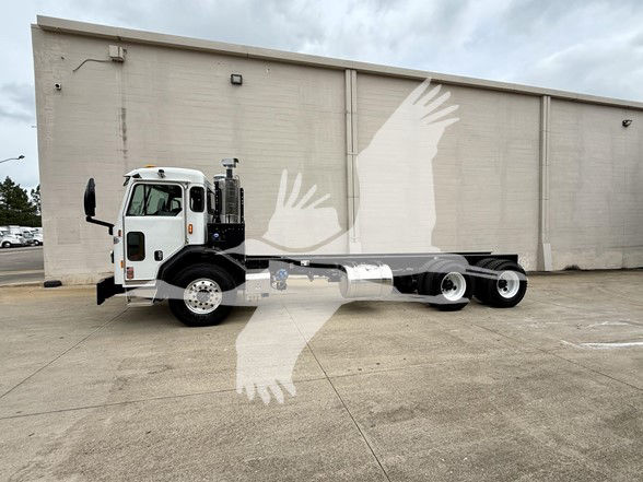 Kenworth L770 cab and chassis truck in a parking lot, white cab, long chassis with dual rear axles, side view showing steering wheel and mirrors