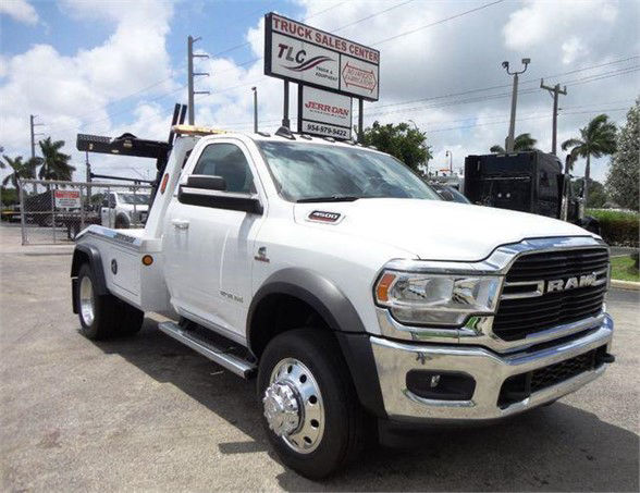 2024 Ram 4500 SLT tow truck with flatbed and dual rear wheels, white paint, chrome grille, RAM emblem, dealership lot in background.