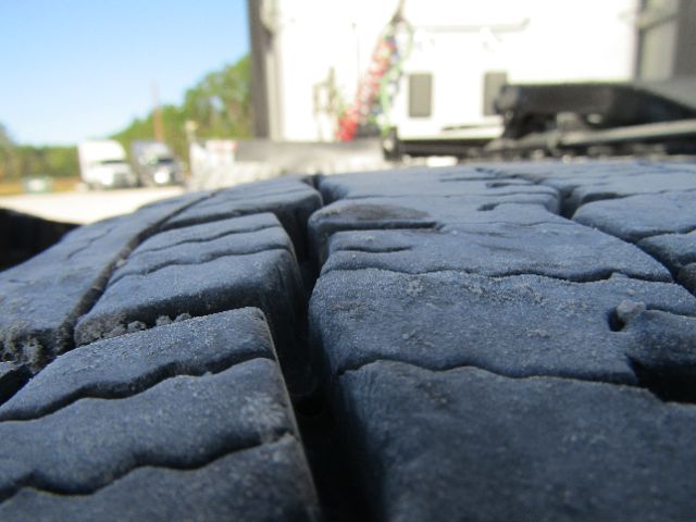 Tire treads up close in foreground with industrial building and equipment in background.