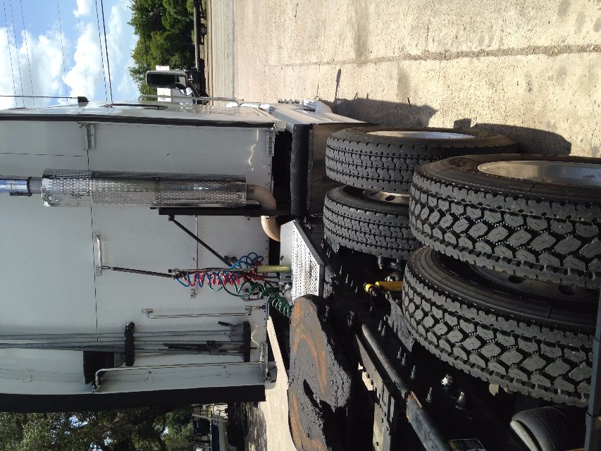 Truck tractor side rear showing dual rear wheels, exhaust stack, air lines, and fifth wheel area.